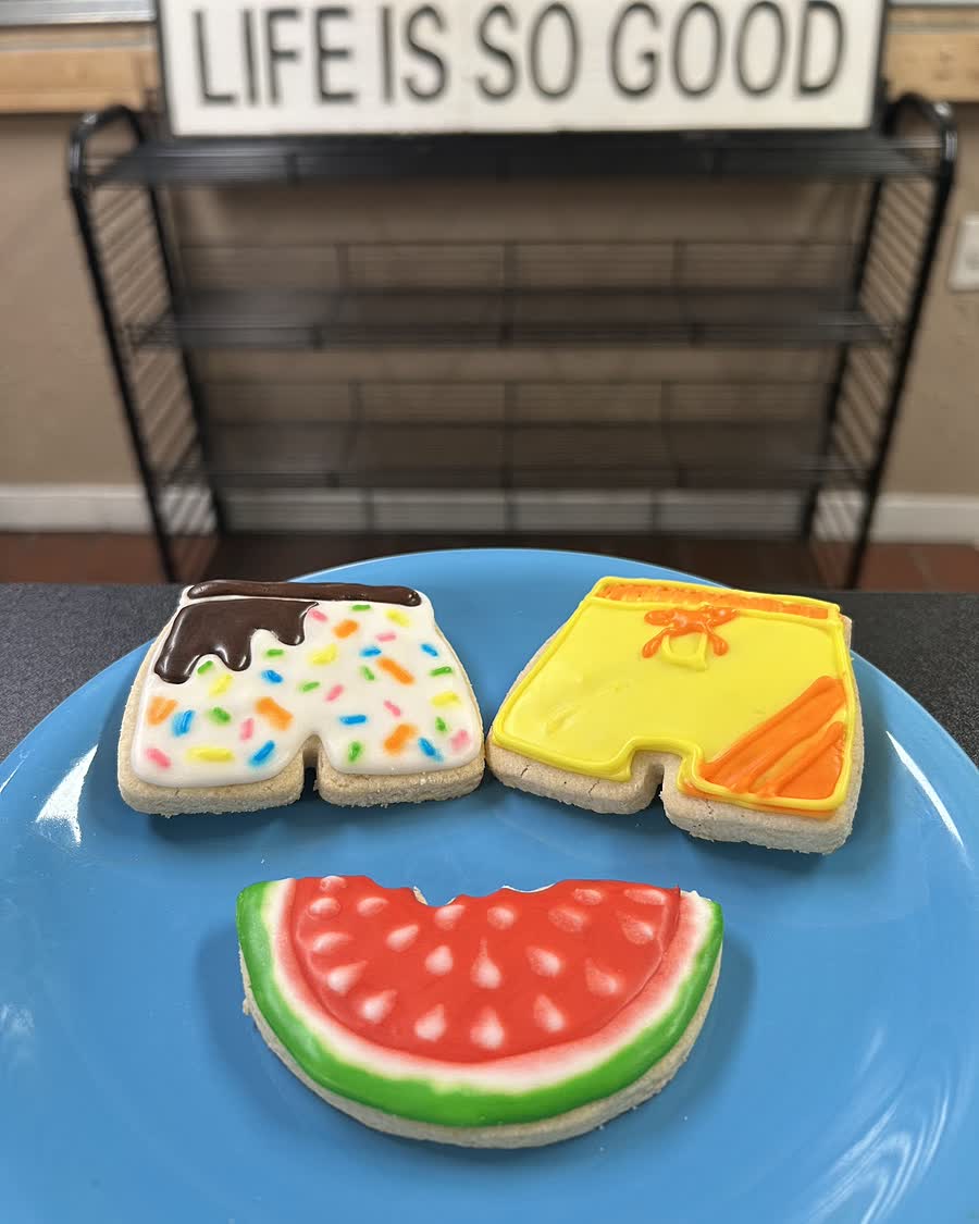 Hand-iced gluten-free sugar cookies on a blue stand inside Bleu Bear Bakery, in front of the shop&rsquo;s &lsquo;Life is so good&rsquo; sign